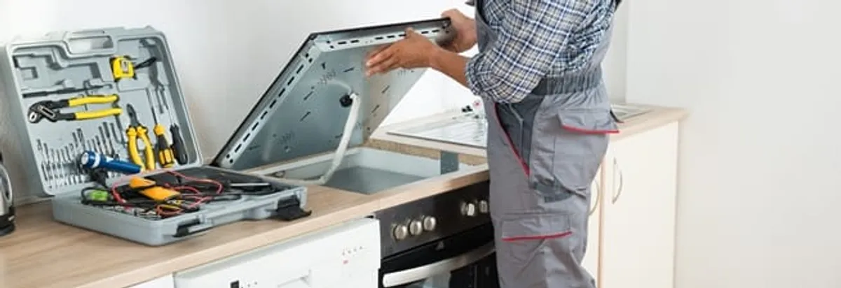 Cooktop repair technician lifting a built-in stovetop for service in Philadelphia, PA