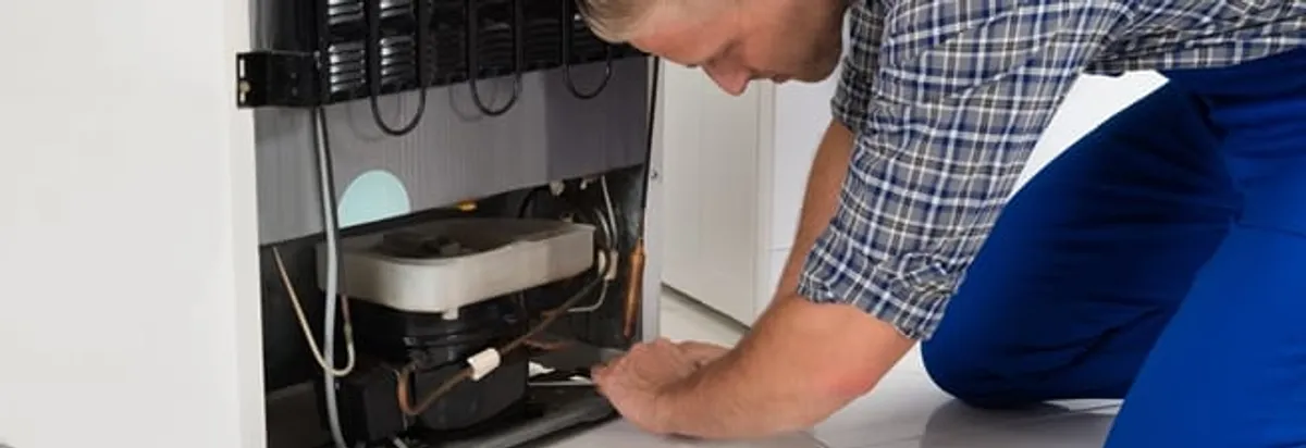 Refrigerator repair technician servicing the compressor and condenser area in Philadelphia, PA