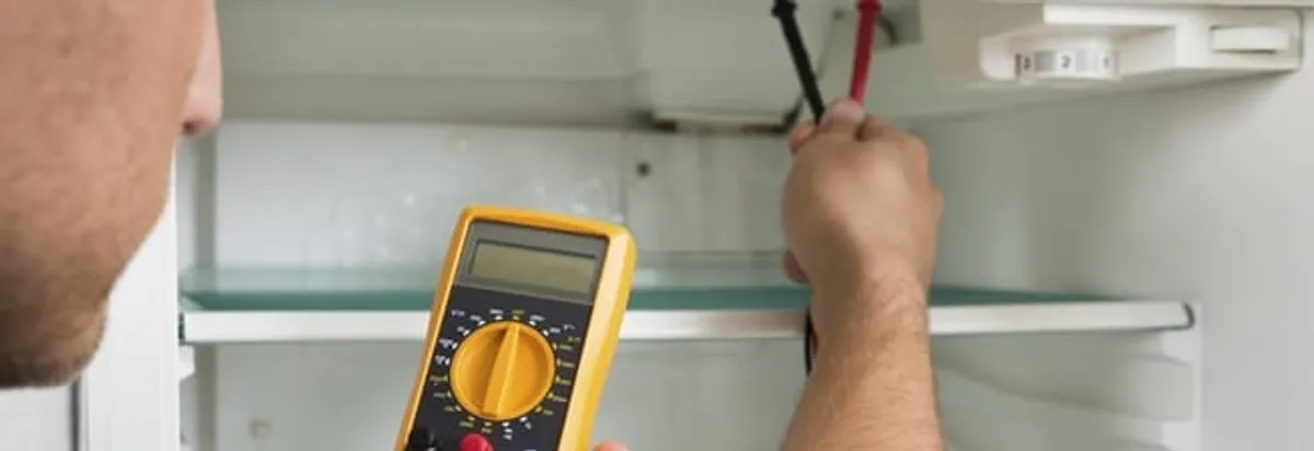 Refrigerator repair technician testing electrical components with a multimeter in Philadelphia, PA