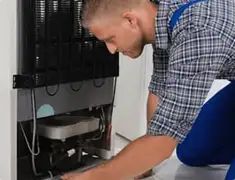 Refrigerator repair technician servicing the compressor and condenser area in Philadelphia, PA